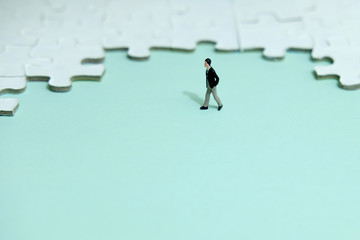 Business strategy conceptual photo - Miniature businessman walking in front of puzzle jigsaw