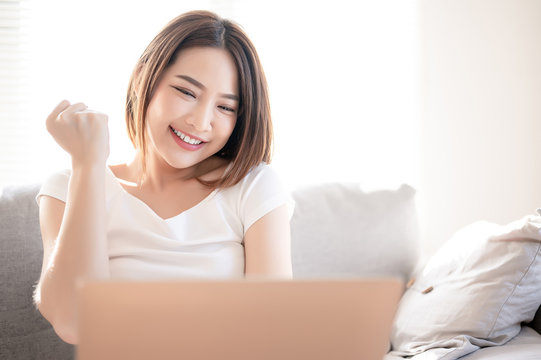 Asian woman glad with something in her laptop in the living room.
