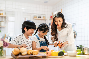 Lovely cute Asian family making food in kitchen at home. Portrait of smiling mother and children...