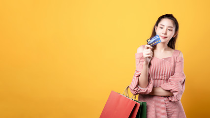 Beautiful asian woman are holding shopping bags with face happily in yellow seamless,isolated background. Shopping lifestyle, online shopping concept.