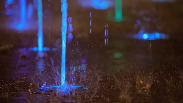 Splashes of fountain. Slow motion of water illuminated in colorful falling on fountain which change it water color in night. Wonderful multicolored fountain throws up high streams of sparkling water.