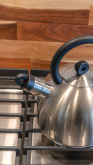 Vertical Kettle on the cooktop against wooden chopping board and tile backsplash