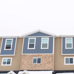 Photo Square Townhouses with snow covered gable roofs against cloudy sky at winter season