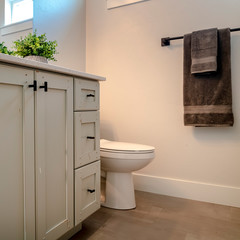 Square Toilet and vanity cabinet inside bathroom with white wall brown floor and window