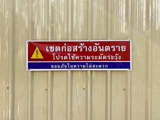 Caution sign on fence of construction site with Thai language 