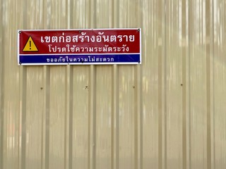 Caution sign on fence of construction site with Thai language " Construction area be  careful sorry for the inconvenience "