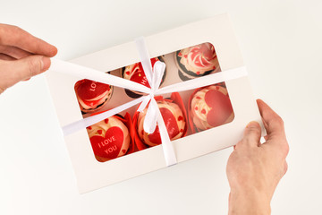 Valentine's day. A set of cupcakes in a box that is unfolded by men's hands, top view.