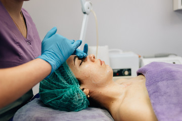 Profile of a woman in a blue cap during a cosmetic procedure, the doctor strokes her face