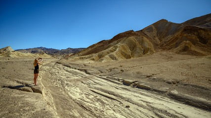 Fototapeta na wymiar Attractive blonde woman standing in the landscape at Zabriskie Point, Death Valley National Park, California, USA