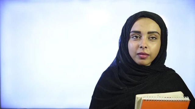 Muslim girl wearing Hijab, hugs orange book and smiling 