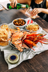 Steamed Giant Mud Crabs, Steamed Flower Crabs and Grilled Shrimps (Prawns) in wooden chopping board with hand pouring beer.