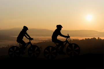 Fototapeta na wymiar Silhouettes Man and Girl are bicycle on mountain in the sunlight