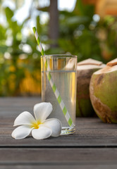 Tropical fresh coconut water in glass decorated plumeria on wooden background