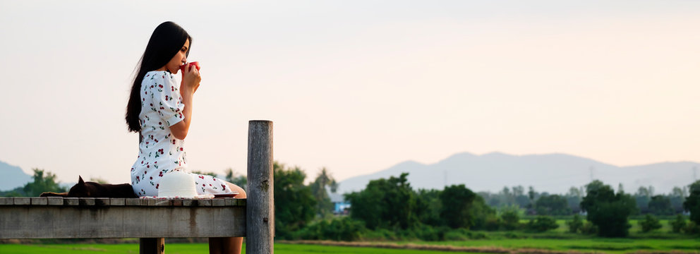 Young woman sits sipping coffee on balcony, looking at nature farmland, panoramic scenery, banner design