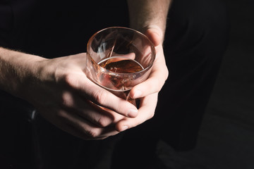 Close-up of the hands of a young man who pours alcohol from a decanter into a glass, on a dark...