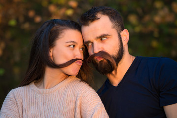 Young beautiful couple in the Park. They fool around and have fun. They make false mustaches out of...