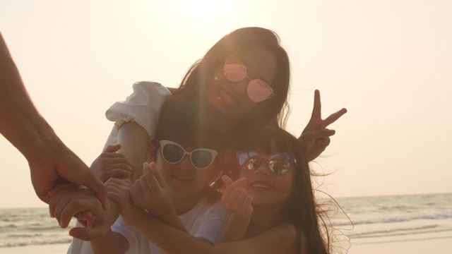 Asian young happy family enjoy vacation on beach in evening. Dad, mom and kid using camera for take selfie while relax together near sea when sunset. Lifestyle holiday vacation summer. 4k Slow motion.