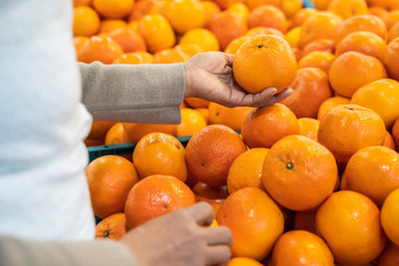 Woman hand choosing orange from the food counter at the supermarket. Shopping for fresh produce.
