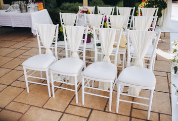 Empty white vintage wooden chairs for the wedding ceremony on brown tile. Summer outdoor event....