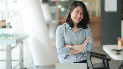Fototapeta premium Portrait of a young businesswoman standing with arms crossed and smiling in the office.