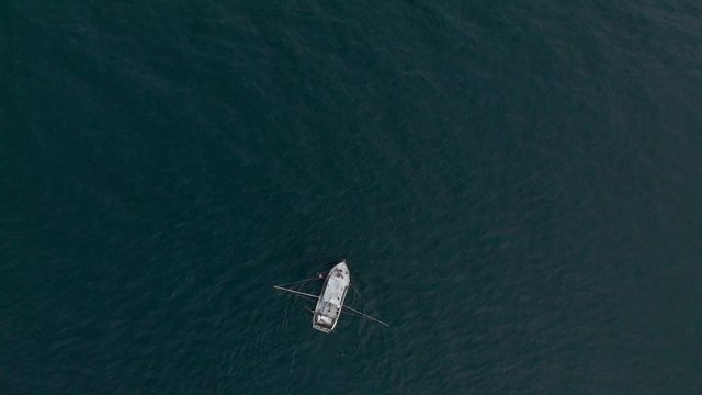 A aerial drone shot of a lone fishing trawler with beautiful clouds and coastline in the distance near Sooke, BC. 4K 24FPS.