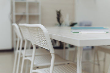 White style. Home comfort. Notebook and pen on a white table with a chair in the office