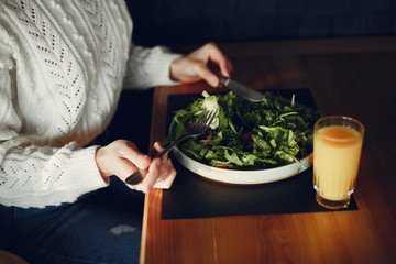 Girl eats vegetable salad. Lady sitting in a cafe. Brunette in a white sweater.