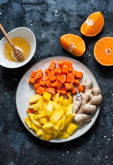 Ingredients for smoothies - fresh ripe mango, carrot, orange, honey, ginger on a dark background, top view. Detox drink