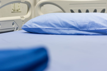 Hospital patients room with adjustable bed, blue pillows and blue blanket.