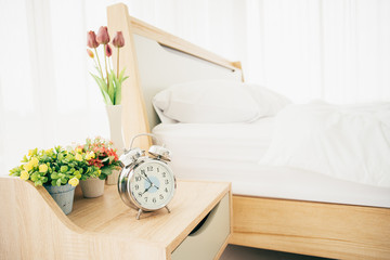 Analog alarm clock on the wooden table over the bed in bedroom, clock almost 8.00 a.m