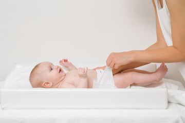 Young mother hands changing diaper for baby on white table. Closeup. Side view.