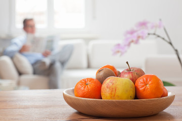 Mature man reading a newspaper on a couch with fruits in the foreground