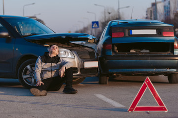 Disappointed man sitting near smashed cars