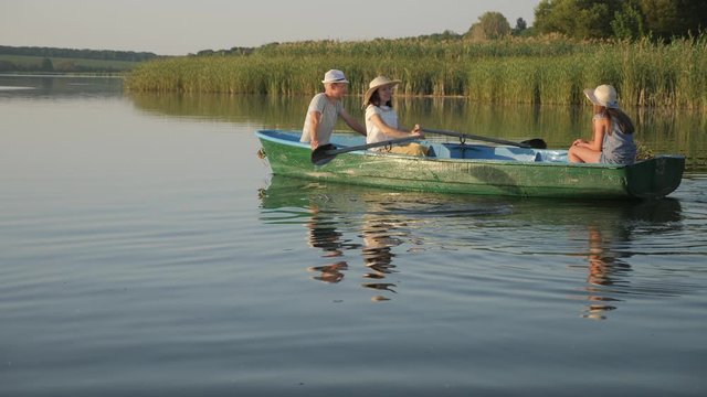 Happy woman with oars in a boat. Young family sails in a wooden boat in a calm rural lake near a forest, slow-motion video
