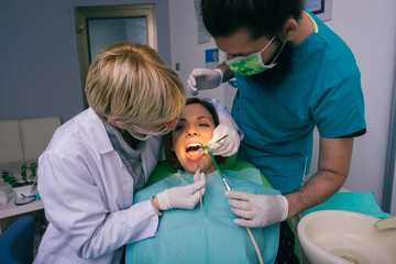 Professional male and female dentists examining woman's teeth in dental office