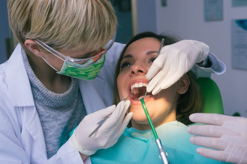 Female dentist in dental office examines the mouth and teeth of a female patient