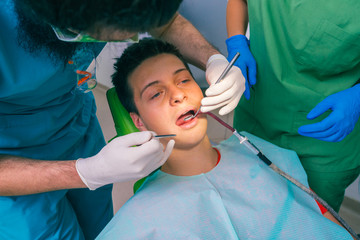 Male dentist with the help of a female dentist examines the mouth and teeth of a teenage boy patient.