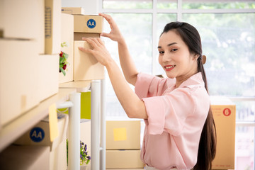 Asian beautiful woman picking up a parcel box from shelves. Online woman vendor and e-commerce concept.