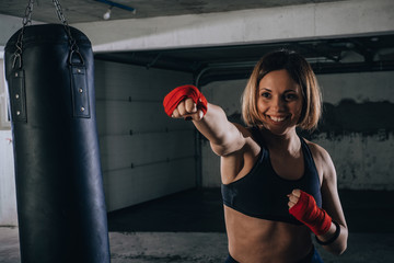 Smiling young beautiful female preparing her bandages for kicking the boxing bag