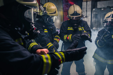 Firemen in uniform wearing gloves and gas masks inside the fire department