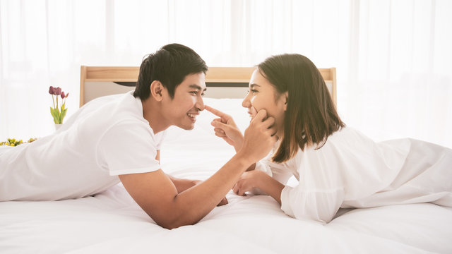 Funny and romantic Asian couple' portrait in bedroom with natural light from window, concept of relationship between husband and wife and being a family.