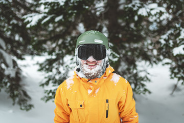 Fototapeta na wymiar Cheerful smiling skier with snow on his bearded face after freeride on mountain forest. Closeup portrait.