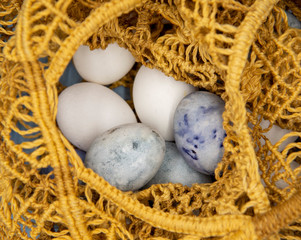 White and painted eggs in a wicker string bag .