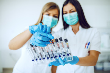 Two dedicated caucasian lab assistants in uniforms, with masks and rubber gloves standing in lab...