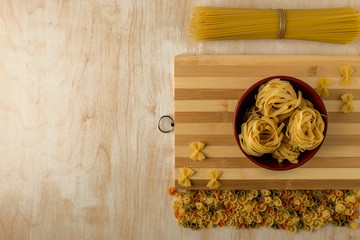 fettucine in a red Cup and farfalla are spread out on a bamboo cutting Board - obrazy, fototapety, plakaty