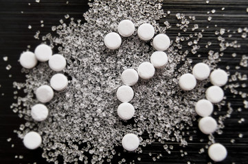 sweetener tablets lying with sugar on a dark background