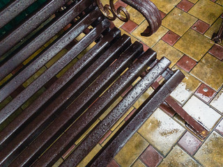 A brown wooden bench with metal legs in raindrops on a yellow paving slab.