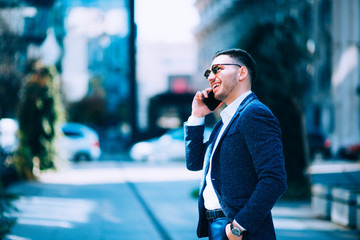 Fototapeta premium Young businessman is walking around and talking on his phone at the city financial center.