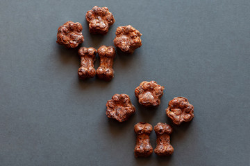Homemade cooking biscuits for dogs, bone- and paw-shaped on dark grey background. Dog and cats treats from liver and carrot. Indoors, copy space, close up, selective focus.