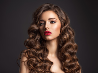Beautiful woman with long brown hair. Beautiful face of an attractive model with red lipstick. Beauty  of curly hair. Closeup portrait  of caucasian stunning girl.